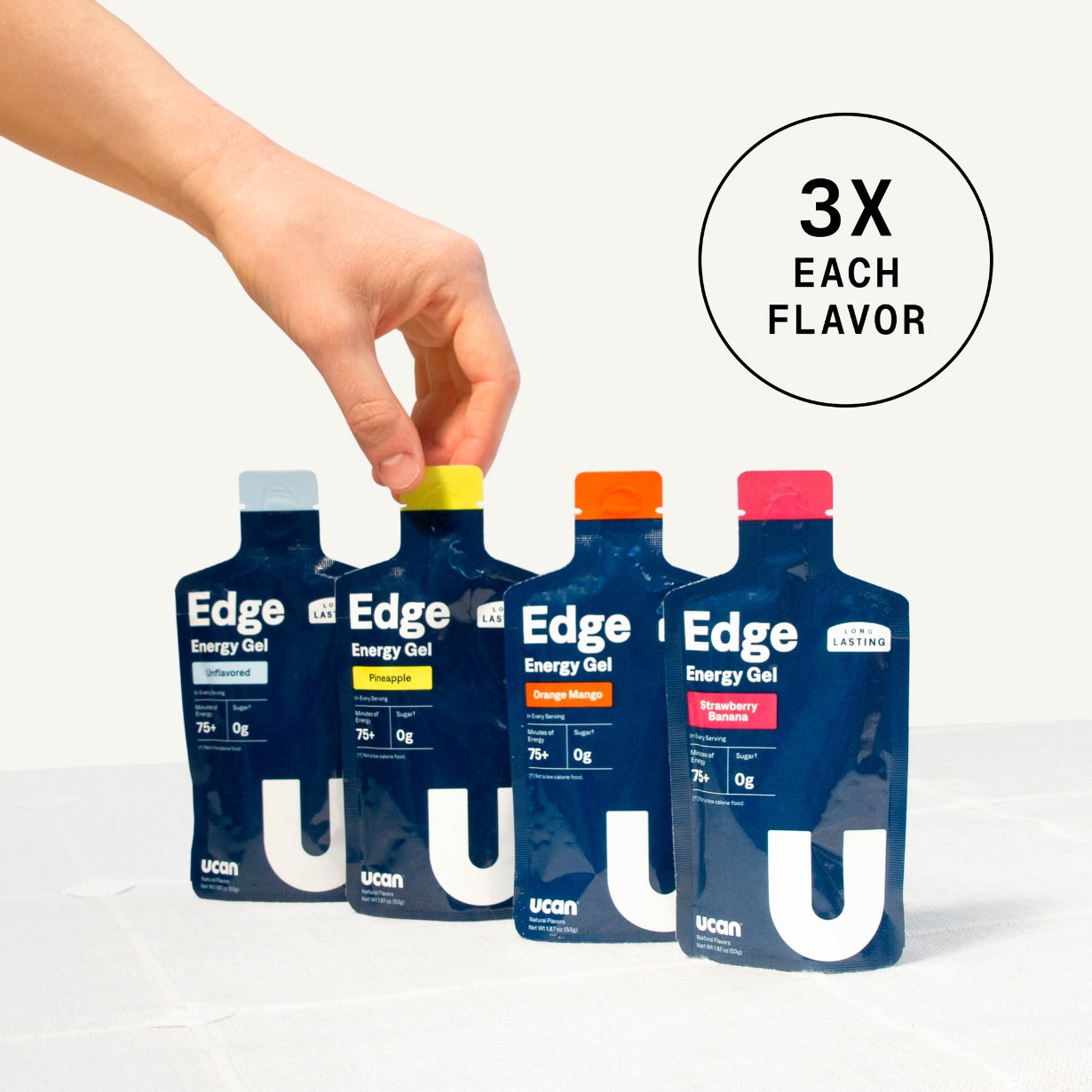 Four Edge Energy Gel pouches in different flavors are lined up on a white surface, with a hand reaching toward the top of the middle pouches. A circular graphic in the upper right reads '3X EACH FLAVOR'.